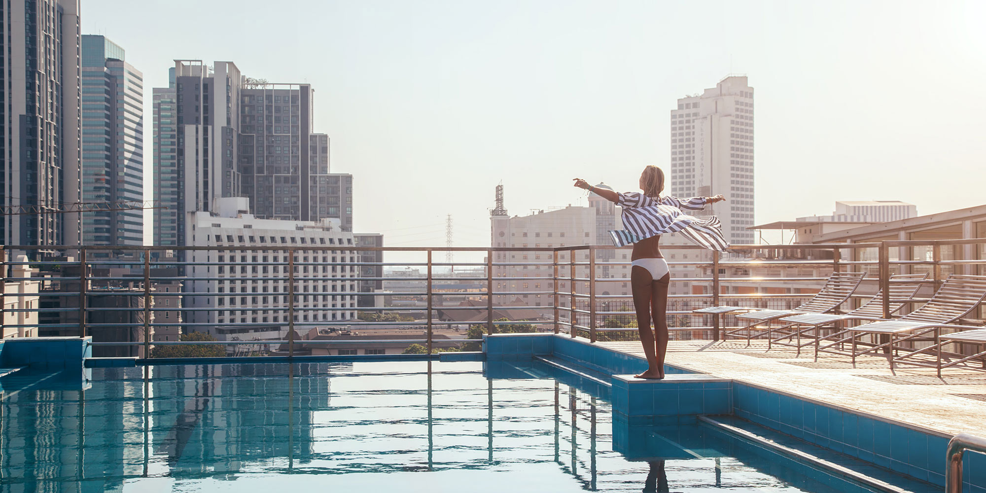 Woman standing beside rooftop pool overlooking downtown