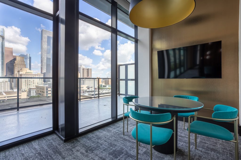 Interior shot of meeting room with table seating, widescreen TV, and floor to ceiling windows with downtown view