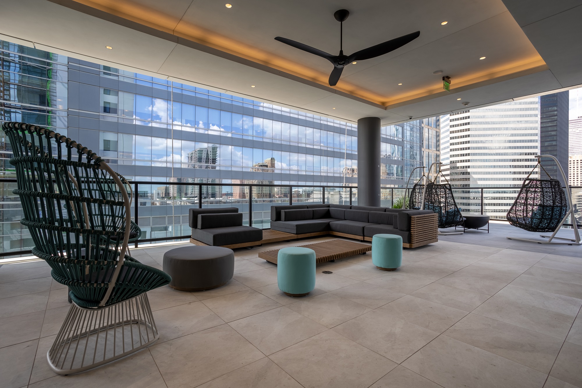 Interior shot of clubhouse with tile flooring, couch and lounge seating, ceiling fan, and floor to ceiling windows with downtown view